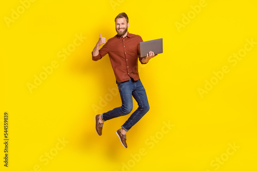 Full body portrait of handsome guy jumping hold netbook show thumb up feedback isolated on yellow color background