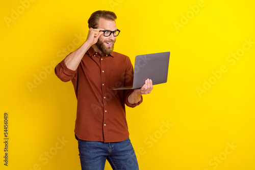 Photo of impressed speechless positive man blond beard burgundy shirt look at laptop touch glasses isolated on yellow color background