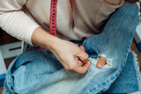 A woman mends jeans, sews a patch on a hole, hands close-up.Mending clothes concept,reusing old jeans.