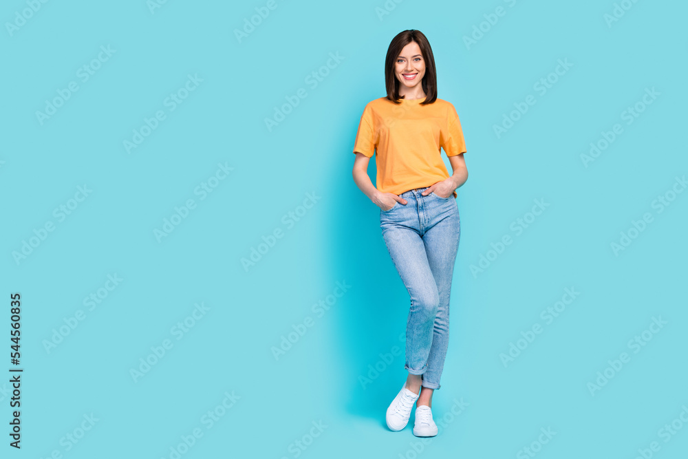 Full size photo of confident friendly girl toothy smile put hands pockets isolated on blue color background Full size photo of confident friendly girl toothy smile put hands pockets isolated on blue color background