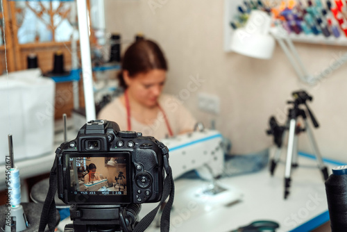 A woman mends jeans, sews a patch on a hole in the home studio and records the broadcast on a camera.Mending clothes concept,reusing old jeans.Small business.Blogging concept.