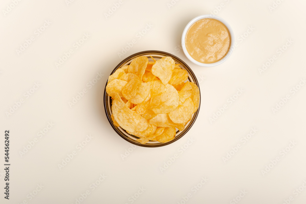 Original salted chips in small glass bowls and sauce from above on a light beige background. 