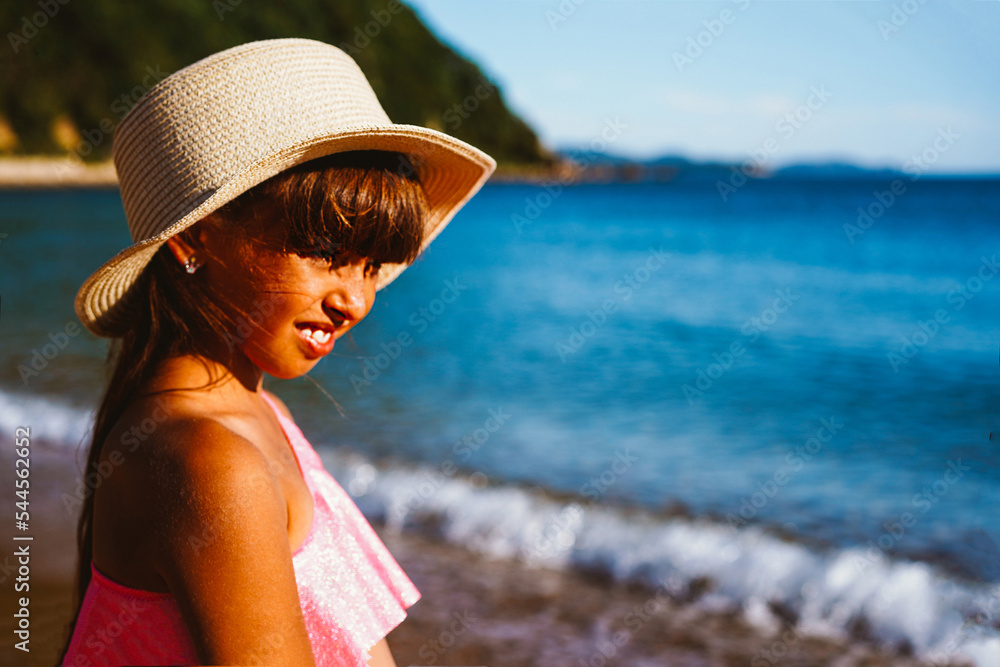 Girl in a hat and swimsuit on the seashore on the beach looks at the horizon