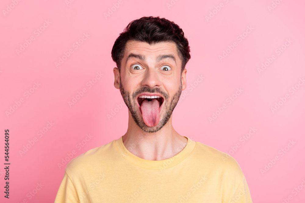 Photo of good mood funky guy with brunet hairstyle dressed yellow t-shirt stick out tongue fooling isolated on pink color background Photo of good mood funky guy with brunet hairstyle dressed yellow t-shirt stick out tongue fooling isolated on pink color background