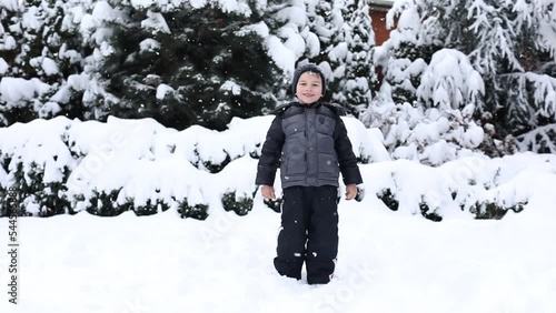 Cute young boy in winter clothes is playing with snow on back yard. Winter time