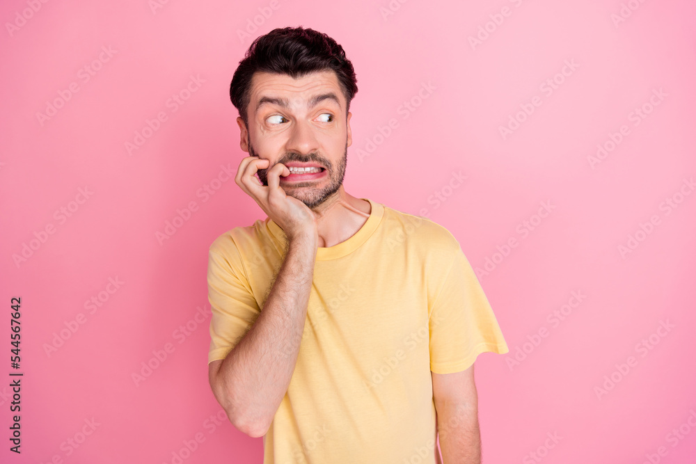 Photo of scared impressed guy with brunet hairstyle yellow t-shirt biting fingers look empty space isolated on pink color background Photo of scared impressed guy with brunet hairstyle yellow t-shirt biting fingers look empty space isolated on pink color background