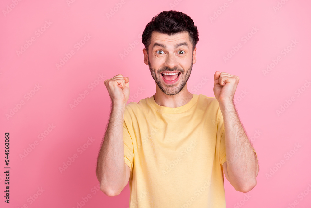 Photo of impressed astonished guy with brunet hair dressed yellow t-shirt clenching fists win lottery isolated on pink color background Photo of impressed astonished guy with brunet hair dressed yellow t-shirt clenching fists win lottery isolated on pink color background