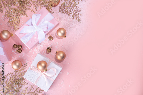 Rose gold Christmas, New Year background with golden christmas tree twigs and balls, holiday gift boxes, decorations, artificial snow, flat lay on pink background copy space