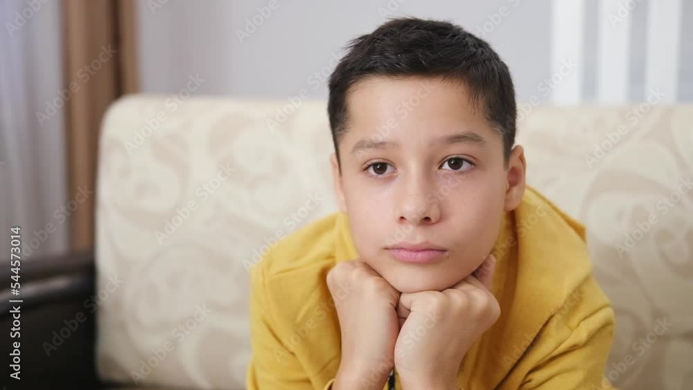 Close up portrait of cute calm smiling dark haired Caucasian teen boy sitting at home in living room on sofa and watching TV. Children's dependence on gadgets, TV and Internet. Close up portrait of cute calm smiling dark haired Caucasian teen boy sitting at home in living room on sofa and watching TV. Children's dependence on gadgets, TV and Internet.