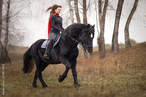 Beautiful girl in red cloak on black stallion