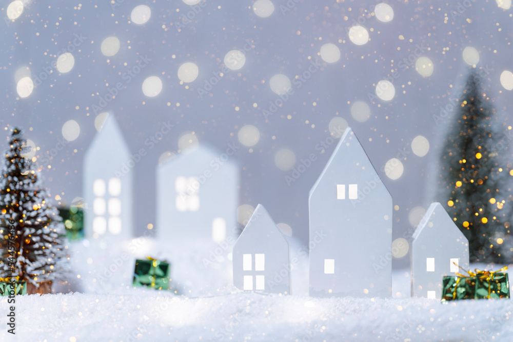 Christmas cute little houses with tree in snow. Glowing festive garland on light background. Cozy fairytale atmosphere with home decor with selective focus in the foreground New Year card. Christmas cute little houses with tree in snow. Glowing festive garland on light background. Cozy fairytale atmosphere with home decor with selective focus in the foreground New Year card.
