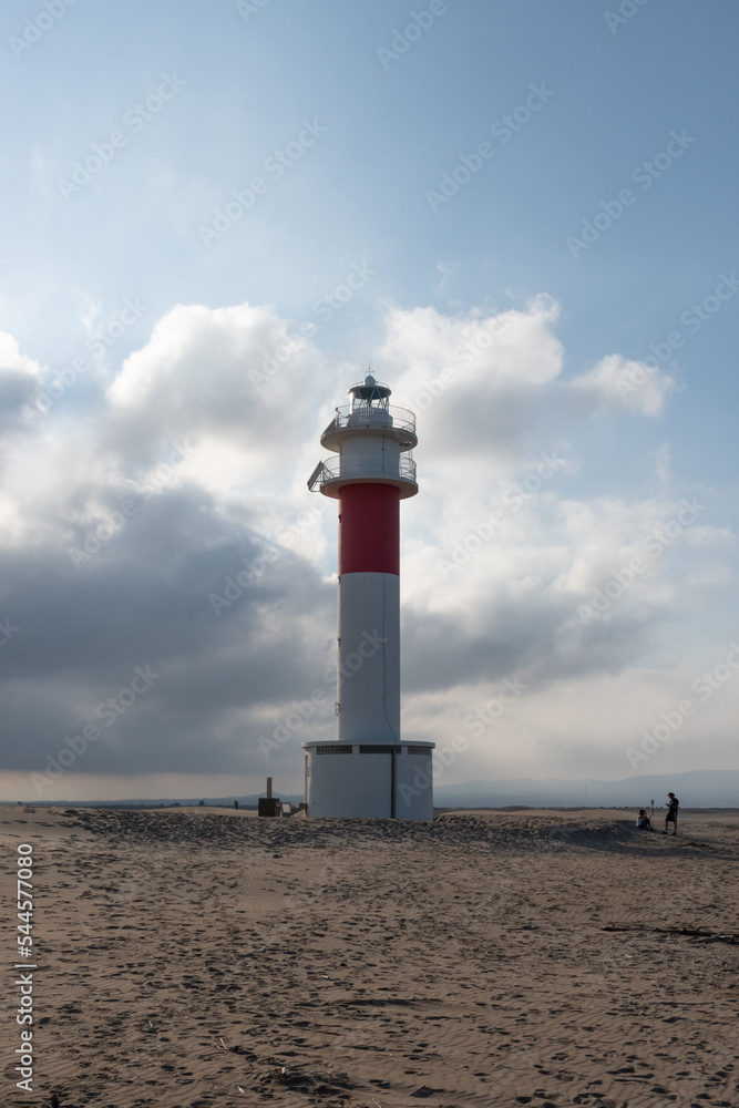 lighthouse in the middle of the beach with a cloudy sky in the background