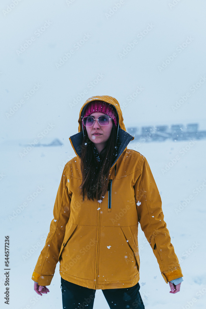 woman in the snow with yellow coat, hat and sunglasses