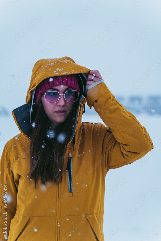 woman in the snow with yellow coat, hat and sunglasses