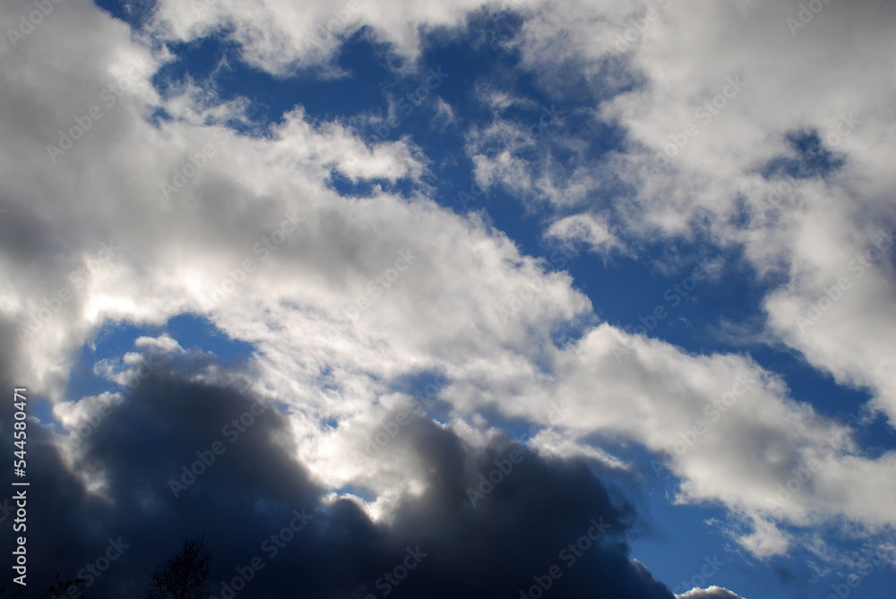 White gray cumulus clouds. Autumn day low fluffy clouds float across the sky. They are snow-white above and dark almost black below due to sunlight and cloud density. Behind them is a blue sky. White gray cumulus clouds. Autumn day low fluffy clouds float across the sky. They are snow-white above and dark almost black below due to sunlight and cloud density. Behind them is a blue sky.