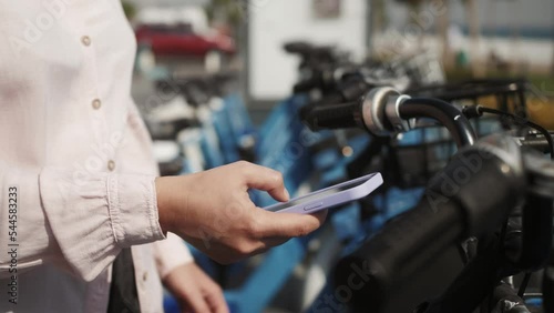 Student girl takes rent bicycle on the parking lot with many rental bicycles for tourists.