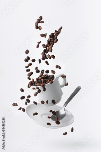 roasted coffee beans spilled from a floating cup and a teaspoon isolated on white background photo