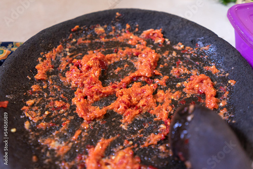 Defocus ground red chili using Indonesian traditional tools called cobek made from stone. photo