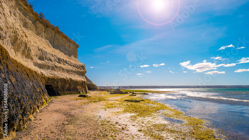 Beautiful and colorful Atlantic coastline in peninsula Valdes near Puerto Madryn with sandstone cliffs at low tide with alga, seashells and caves, Patagonia, Argentina, with direct sunlight lens flare photo
