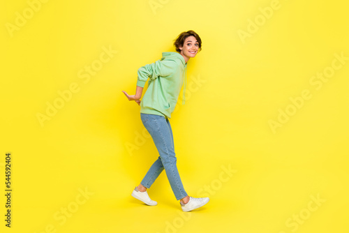 Full length photo of funny pretty girl dressed green sweatshirt stealing arms empty space isolated yellow color background