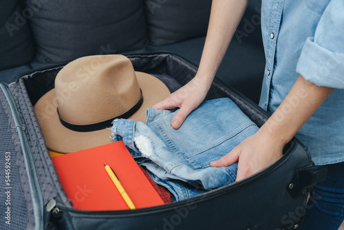 Road trip wanderlust lifestyle concept. Side view of female hands neatly packing and organizing suitcase. Stack clothing for sorting and baggage packing. Ready for vacation. Travel blogger essentials