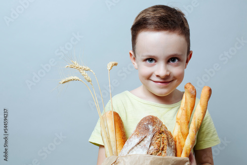 child with a grocery bag with freshly baked bread and ears of wheat, smiling softly. close up