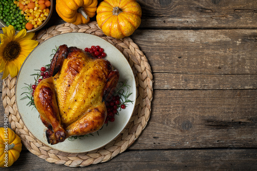 Happy Thanksgiving holiday background. Roasted whole chicken or turkey with autumn vegetables for thanksgiving dinner on wooden table. Copy space