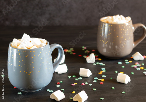 Two cups of cocoa with marshmallows on dark background with small snowflakes