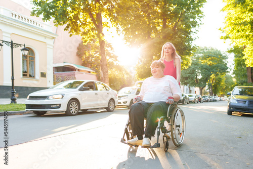 Young female caregiver pushing wheelchair with female person with disability across city street © fotofabrika