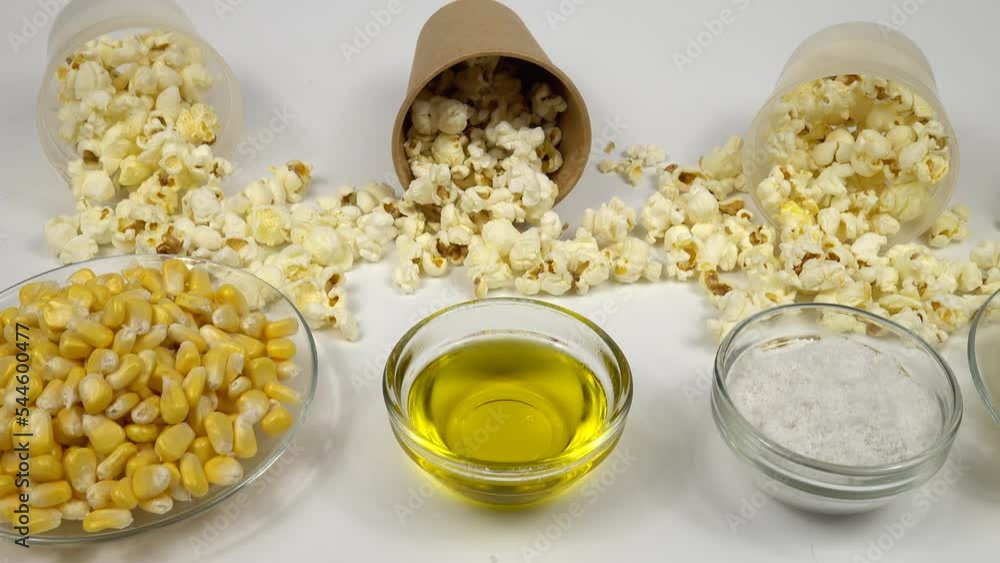 Ingredients for making salted popcorn. Salt, vegetable oil, fresh corn kernels and ready-made popcorn pop corn in the paper cups on a white table Ingredients for making salted popcorn. Salt, vegetable oil, fresh corn kernels and ready-made popcorn pop corn in the paper cups on a white table