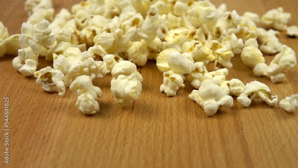 A lot of white salty popcorns fall on a wooden board, background, slow motion A lot of white salty popcorns fall on a wooden board, background, slow motion
