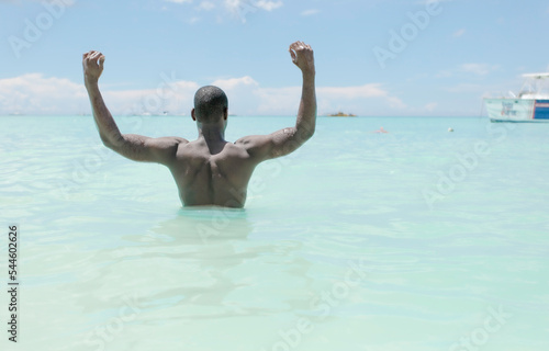 Black man from behind with arms raised in the sea