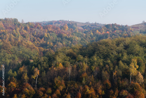 Hills covered with colorful forest in autumn and village houses on top of hills, rural landscape