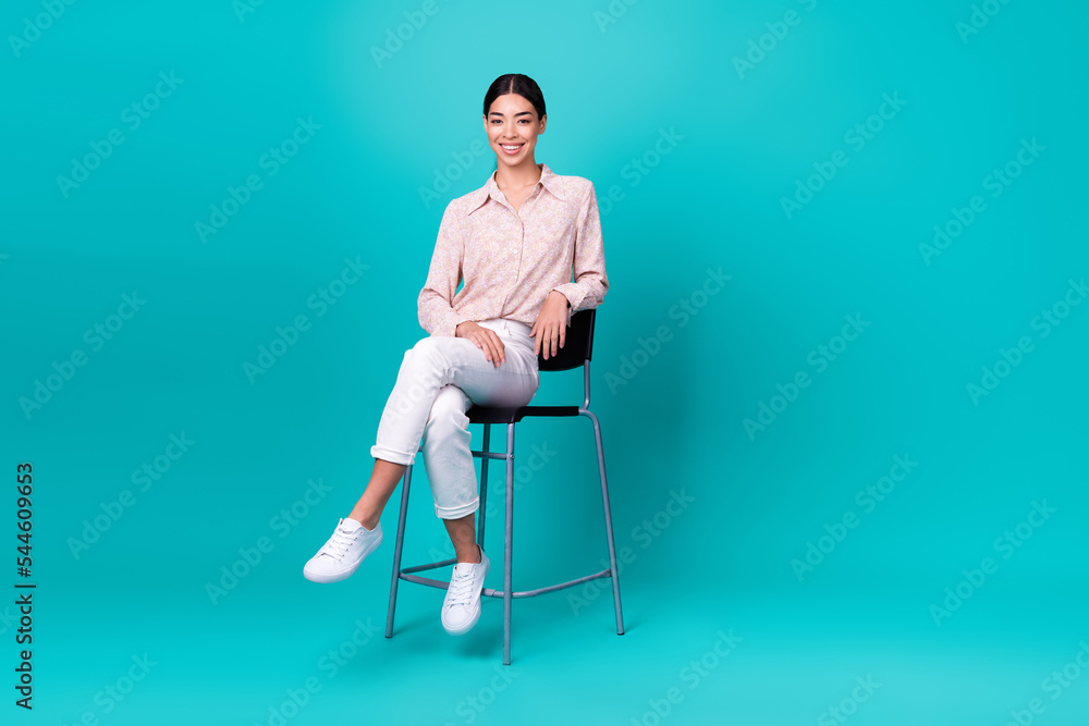 © deagreez - Full size photo of young korean lady sit bar chair relaxing toothy smile wear stylish smart casual outfit isolated on cyan color background