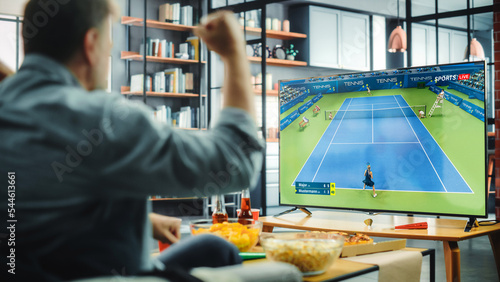 At Home Tennis Fans Sitting on a Couch Watch Game on TV. Celebrate when Favourtite Sportsperson Win the Championship. Screen Shows Professional Players During World Cup. Over the Shoulder photo