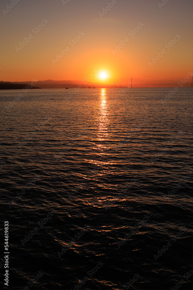 Fototapeta premium Orange sunset sky and sun over the sea. Water surface and outlines on the horizon.