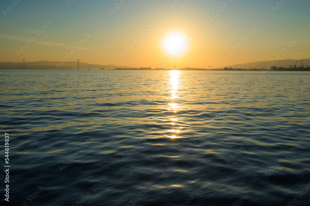 Fototapeta premium Orange sunset sky and sun over the sea. Water surface and outlines on the horizon.