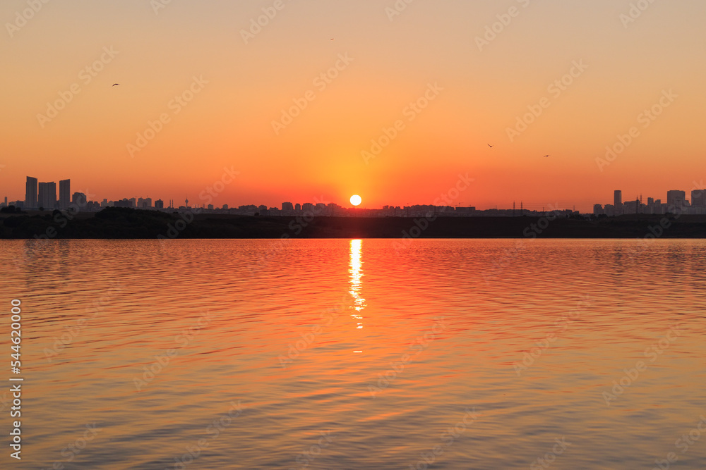 Orange sunset sky and sun over the sea. Water surface and outlines on the horizon.