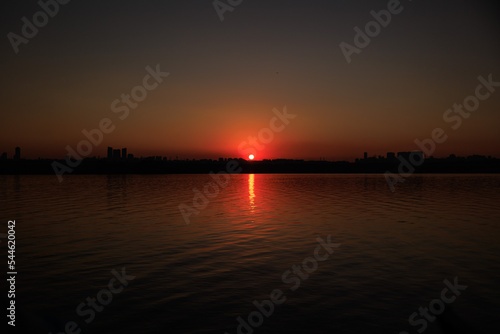 Orange sunset sky and sun over the sea. Water surface and outlines on the horizon. © Kozlik_mozlik