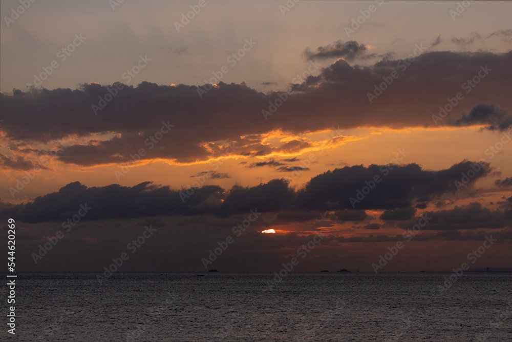 Orange sunset sky and sun over the sea. Water surface and outlines on the horizon.