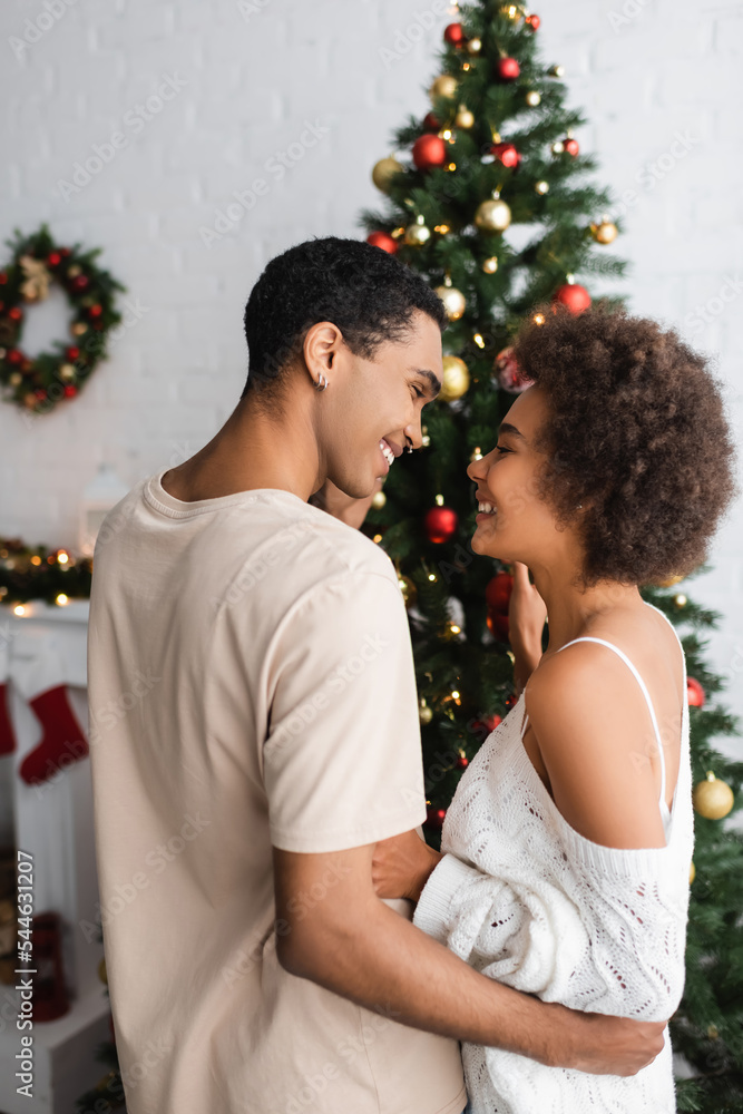 young african american couple smiling at each other near decorated christmas tree