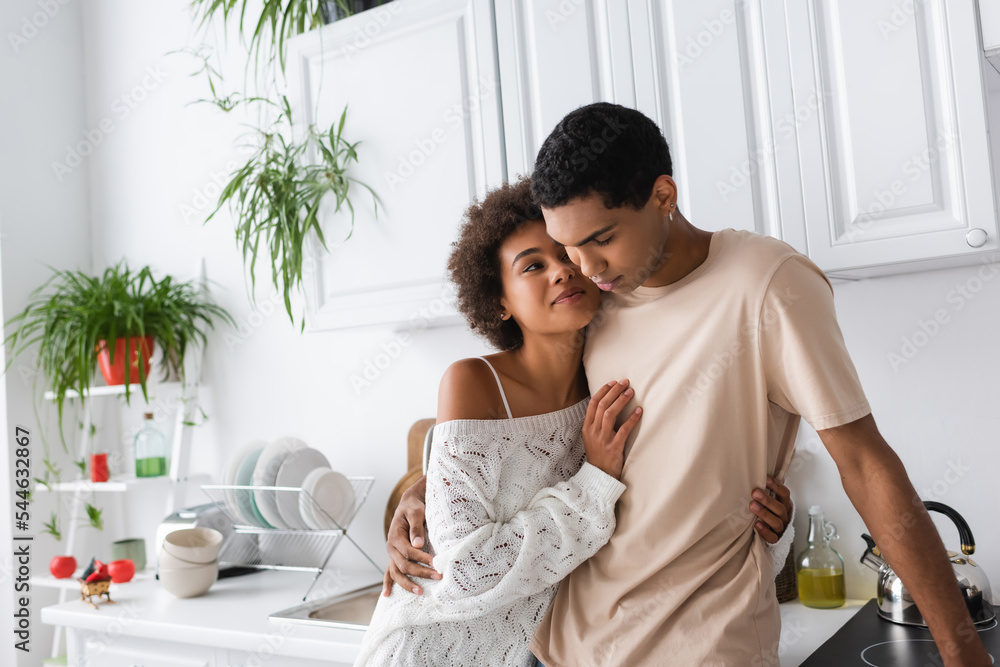 sexy african american woman in white knitted sweater smiling near young boyfriend in kitchen sexy african american woman in white knitted sweater smiling near young boyfriend in kitchen