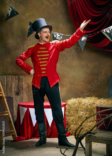 Принти на полотні Vintage portrait of male retro circus entertainer expresses rejoice and announces start of show over dark retro circus backstage background