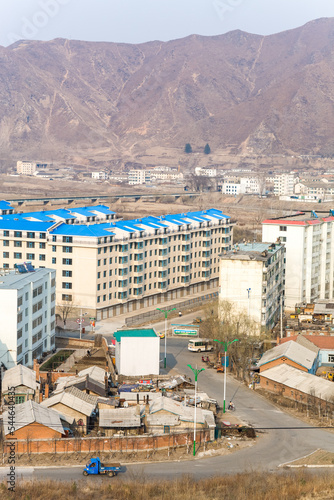 TUMEN, JILIN PROVINCE, CHINA - April 2008: contrast between modern Tumen buildings with blue roofs and North Korean countryside, near Namyang, in the background, Yanbian Korean Autonomous Prefecture photo