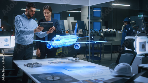 Aeronautics Factory Office Meeting Room: Engineer Holds Tablet Computer, Showing Augmented Reality Airplane Jet Engine to a Female Manager. Modern Industry 4.0 Research and Development Test. photo