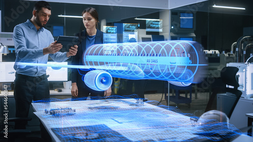 Aeronautics Factory Office Meeting Room: Engineer Holds Tablet Computer, Showing Augmented Reality Airplane Jet Engine to a Female Manager. Modern Industry 4.0 Project Research and Development Test. photo