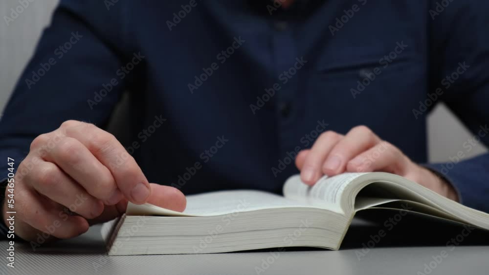 man in a blue shirt is reading a book. the human fiddles with the pages of the book and takes off his glasses, putting them on the book. rest break. close up. man in a blue shirt is reading a book. the human fiddles with the pages of the book and takes off his glasses, putting them on the book. rest break. close up.