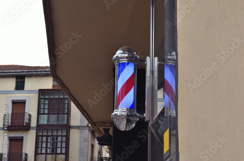 Poste de barbero azul, blanco y rojo con cromados y de fondo un edificio