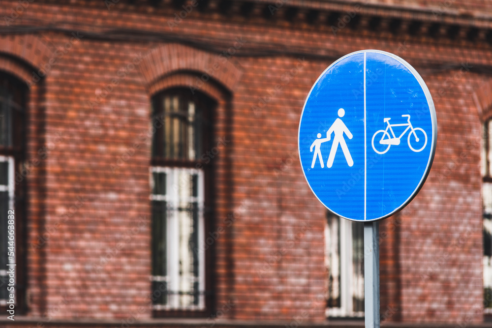 Obraz premium Blue round traffic road sign that shows a lane dedicated for pedestrians and bicycles in front of a brick building in an urban area