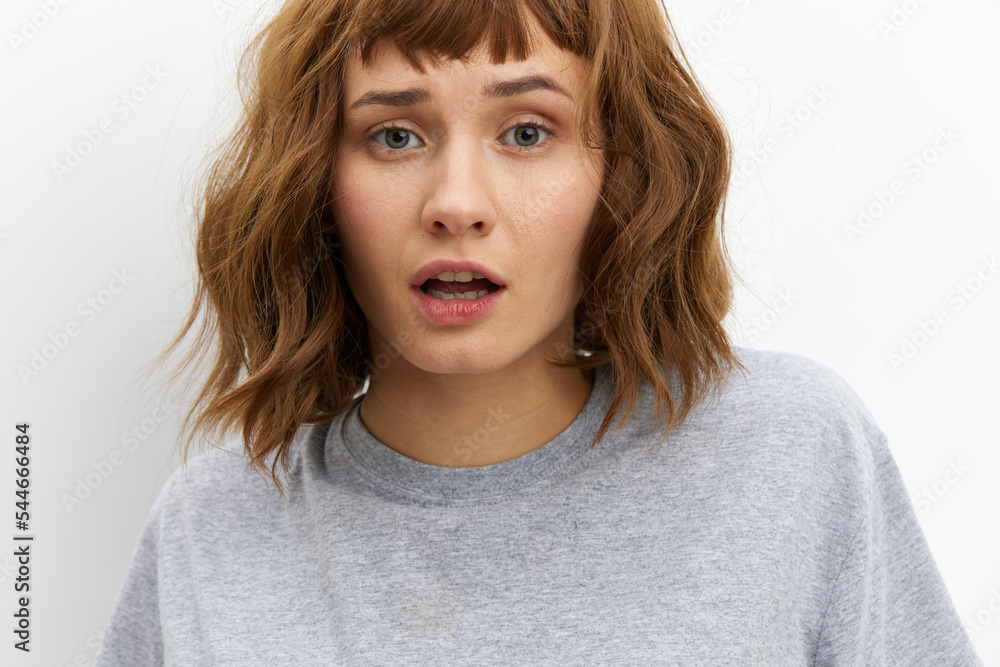 a sweet, inspired, beautiful red-haired, curly-haired woman stands on a white background in a gray cotton T-shirt and looks at the camera with a gentle gaze